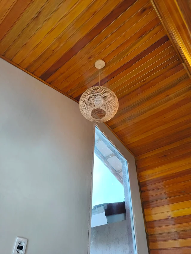 Luminária pendente próxima a uma escada sob um forro de madeira.